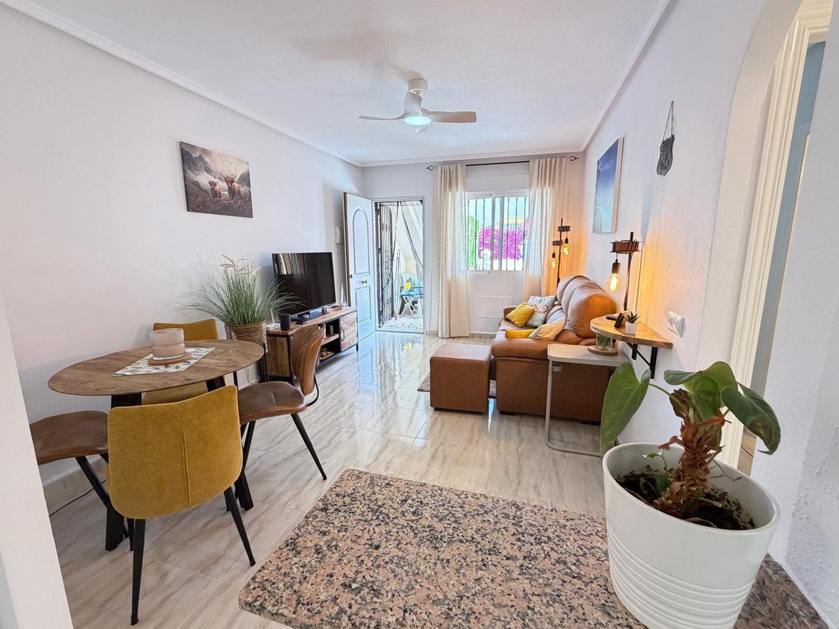 A modern living and dining area with yellow chairs, a leather sofa, and access to an outdoor space with vibrant flowers visible through the window.
