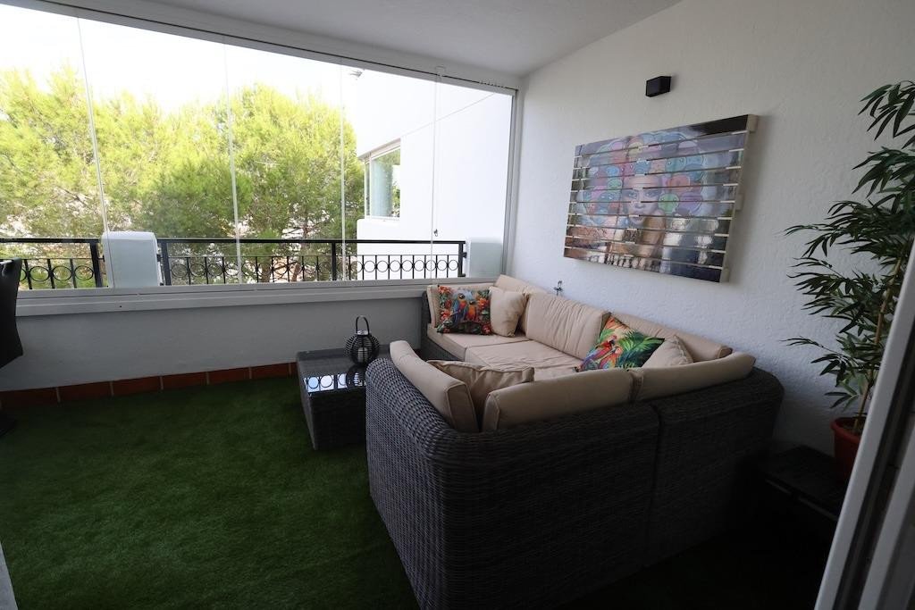 Comfortable wicker sofa and coffee table on a covered terrace with artificial grass and tree views.