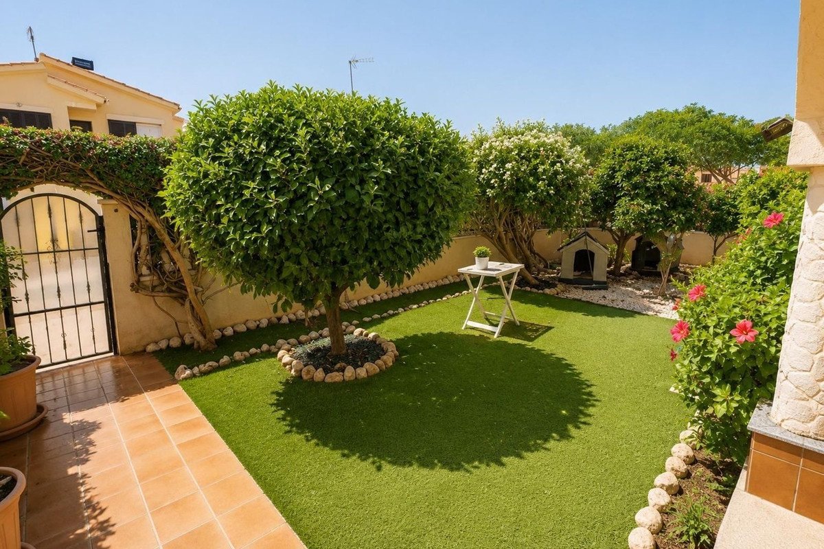 Artificial grass garden with trees, dog house, and a small table. Sunny day with blue sky.