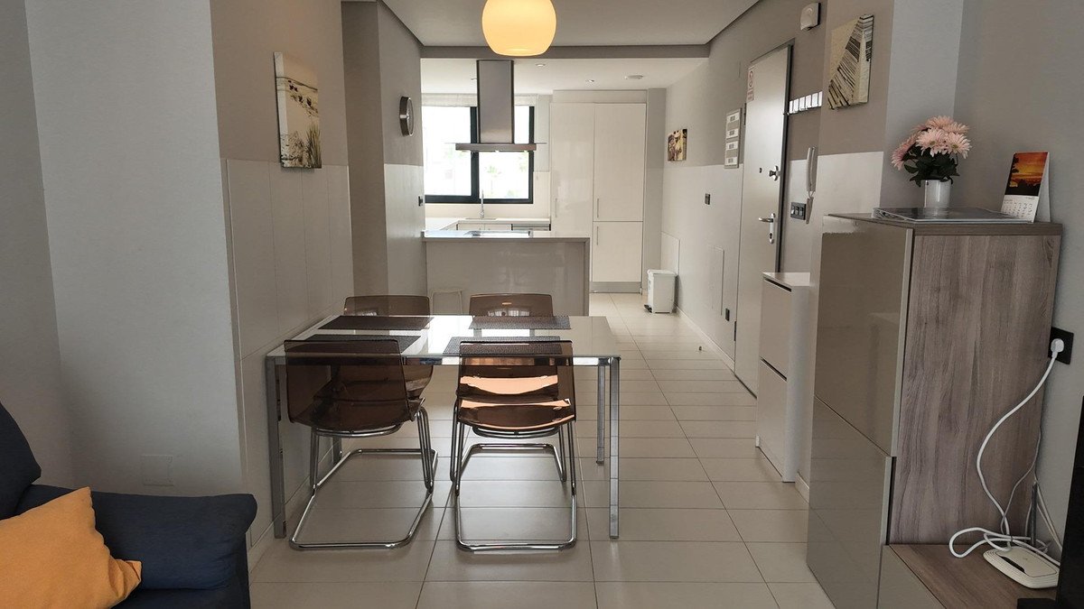 Dining area with glass table, chairs, and kitchen view in a modern apartment