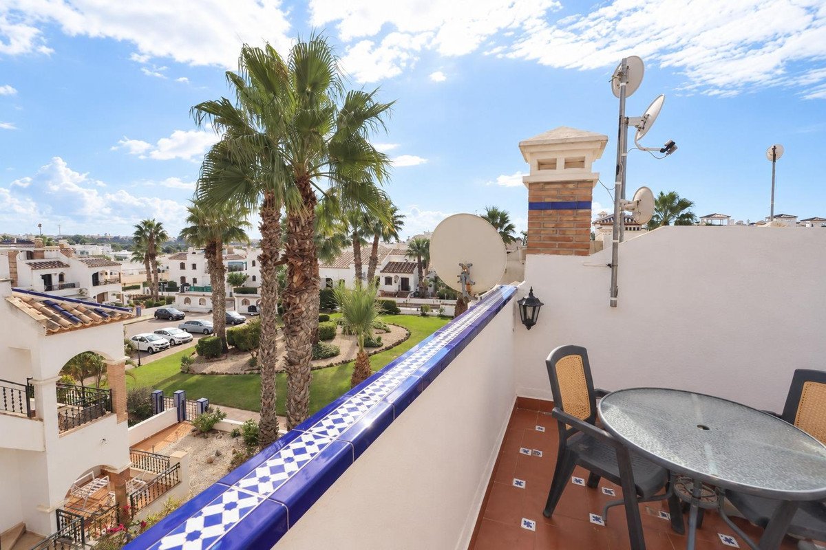 Terrace with table and chairs overlooking palm trees and white residential buildings under a blue sky.