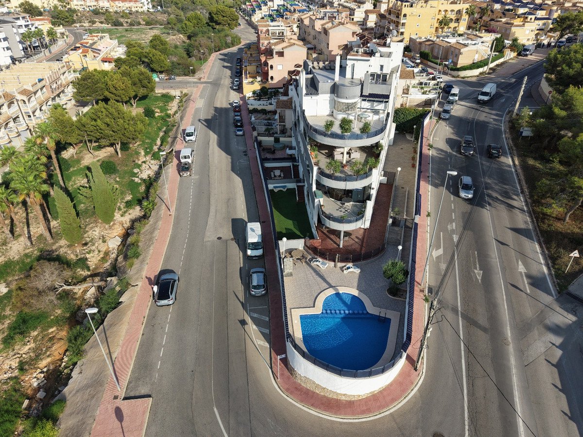 Modern building with a curved facade, featuring balconies, a swimming pool, and a street with cars in a residential area.