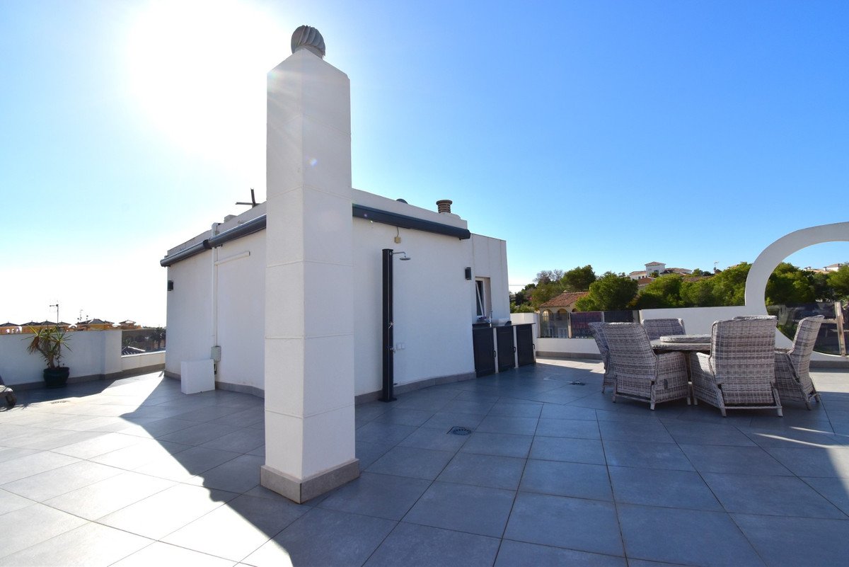Spacious terrace with outdoor dining set, chimney, and distant houses under a clear blue sky.