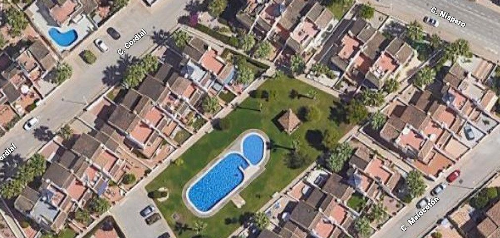 Aerial view of a residential complex featuring a large, uniquely shaped swimming pool and green spaces.