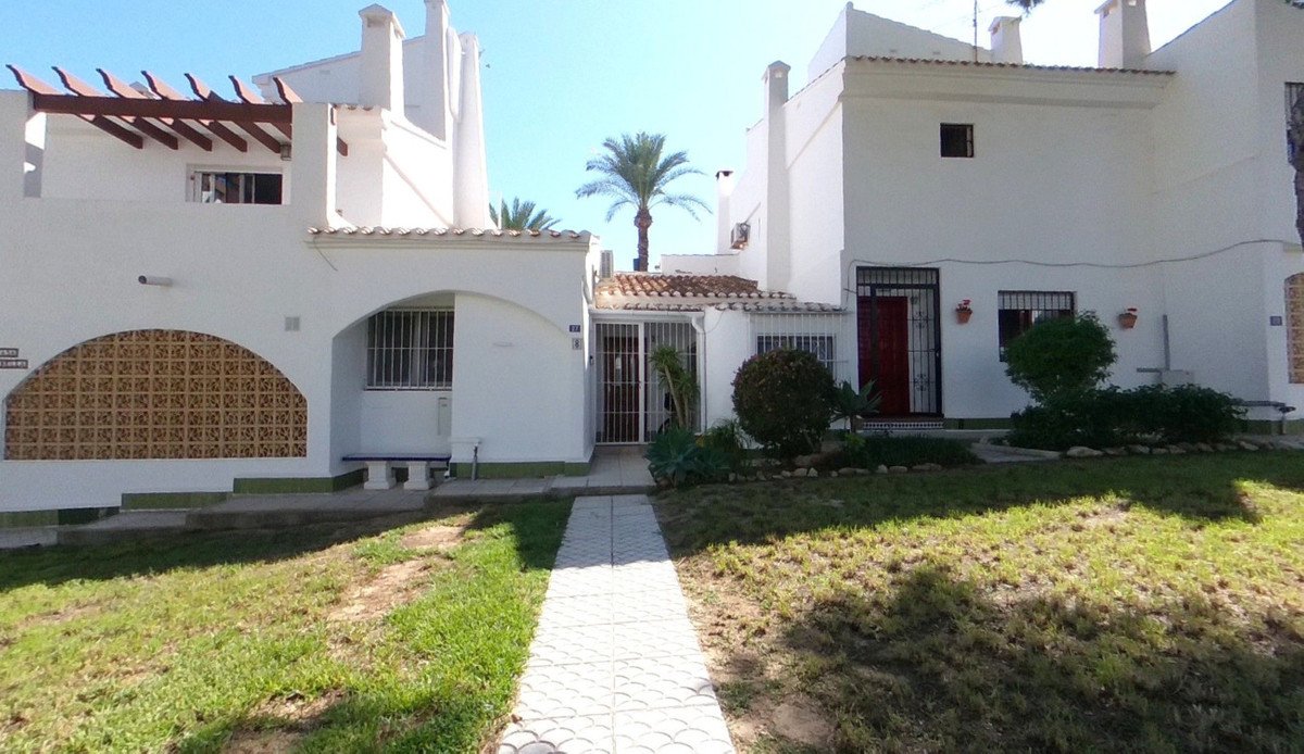 Exterior of a white townhouse with a garden, pathway, palm trees, and a pergola-covered section on the left.
