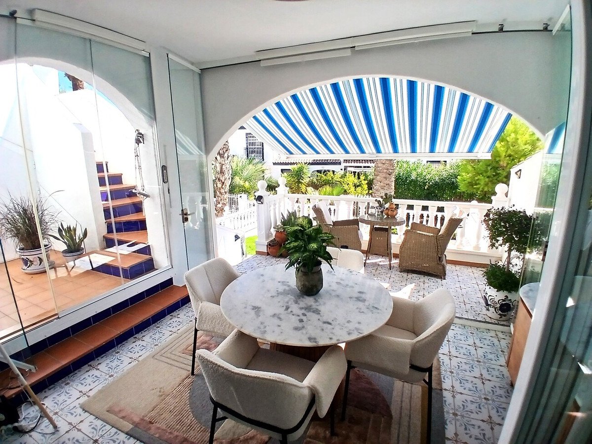 Sunroom with marble dining table and chairs, opening to a balcony with outdoor seating and blue striped awning.