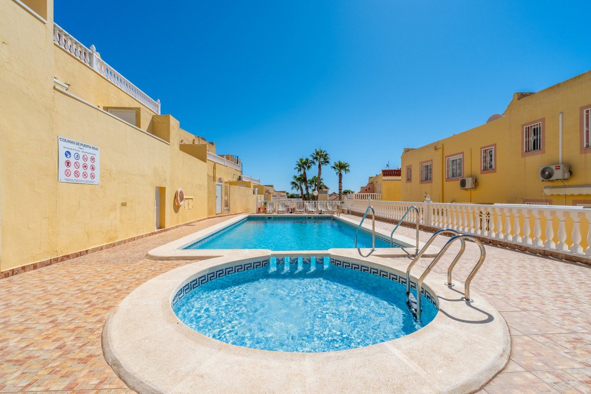Outdoor swimming pool and jacuzzi area with palm trees and yellow buildings under a clear blue sky.