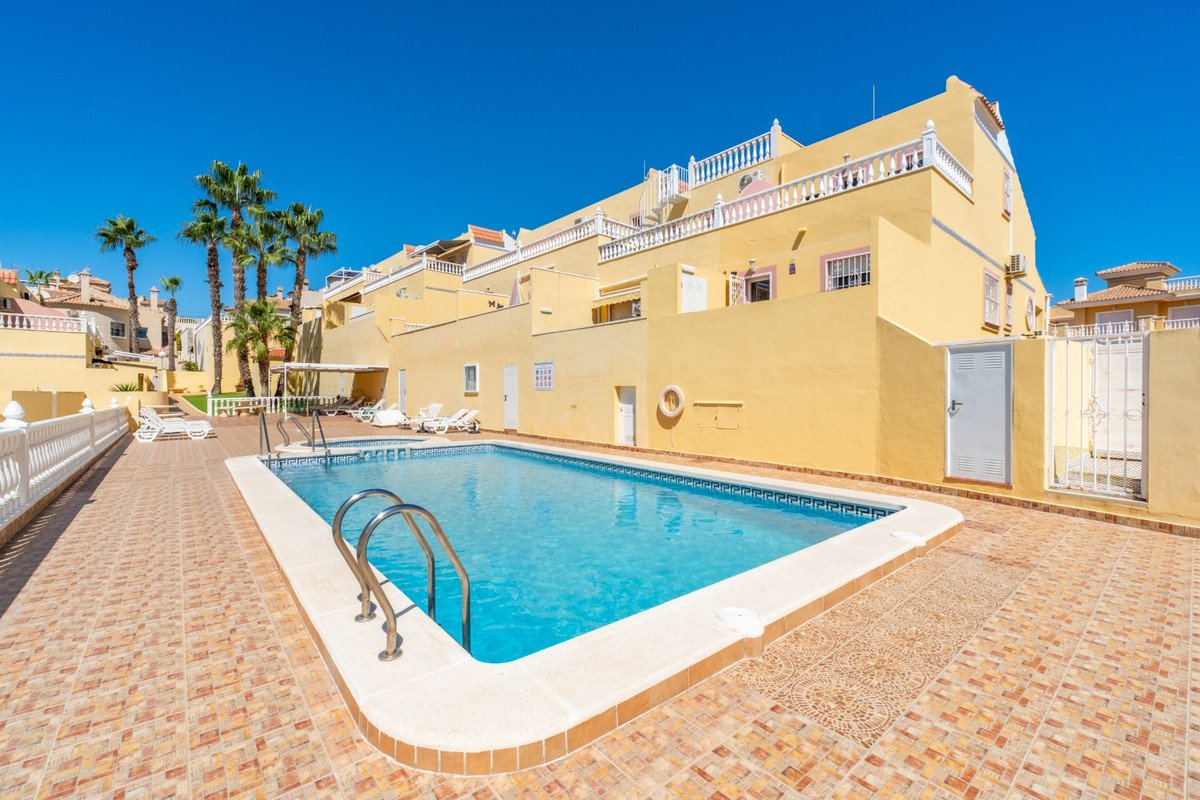 Sunny exterior of a townhouse with a swimming pool and palm trees under a clear blue sky.