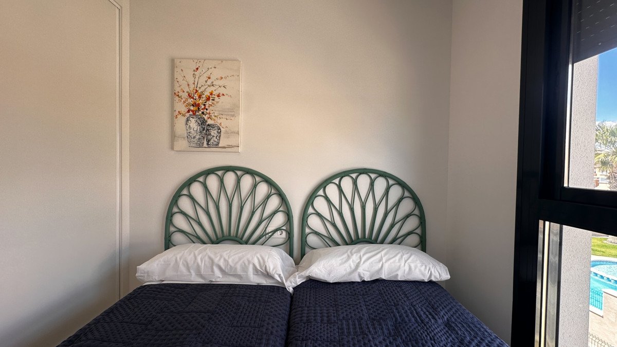 Two single beds with dark blue comforters and white pillows, decorated with a floral painting. View of a pool through the window.