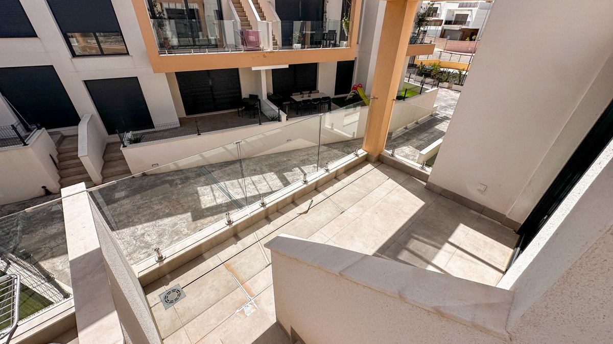 A modern terrace with a glass balcony overlooking an outdoor courtyard with stairs and a small slide visible on the upper level.