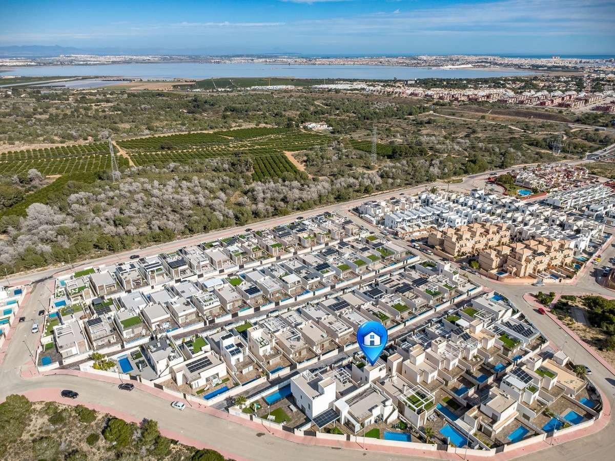 Aerial view of a modern villa complex with private pools, overlooking a lake and distant city.