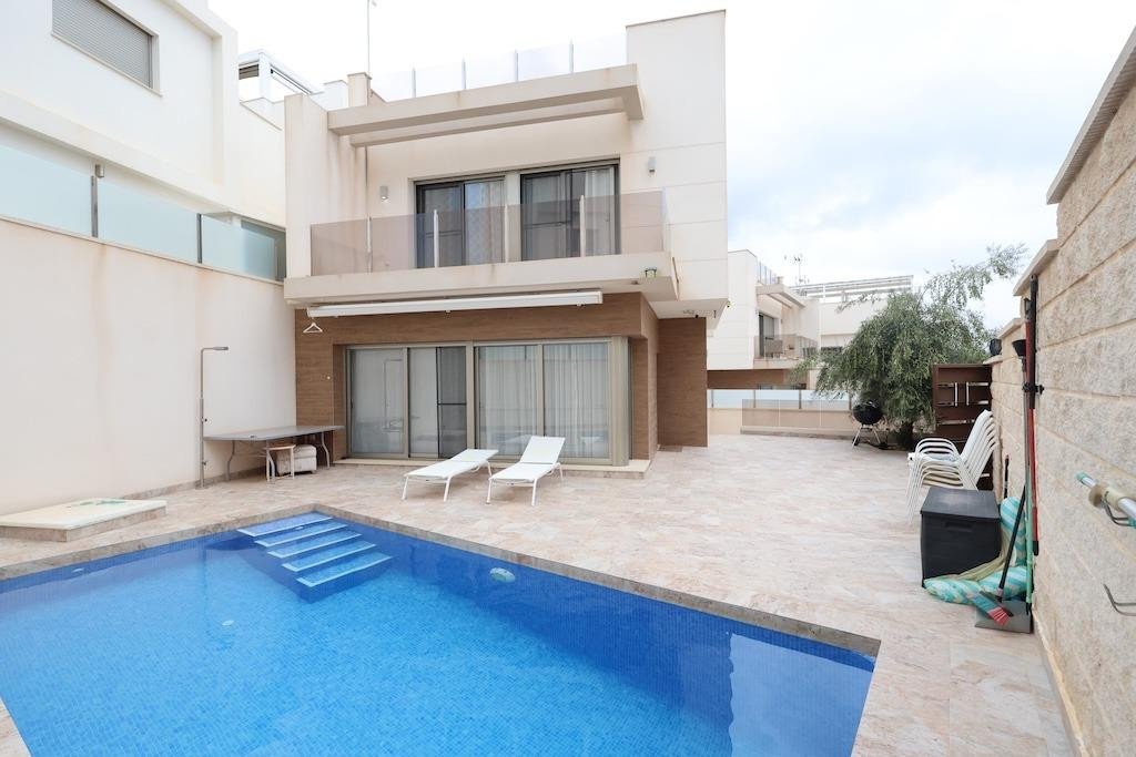 Modern house exterior with a private swimming pool, sun loungers, and a paved patio area.