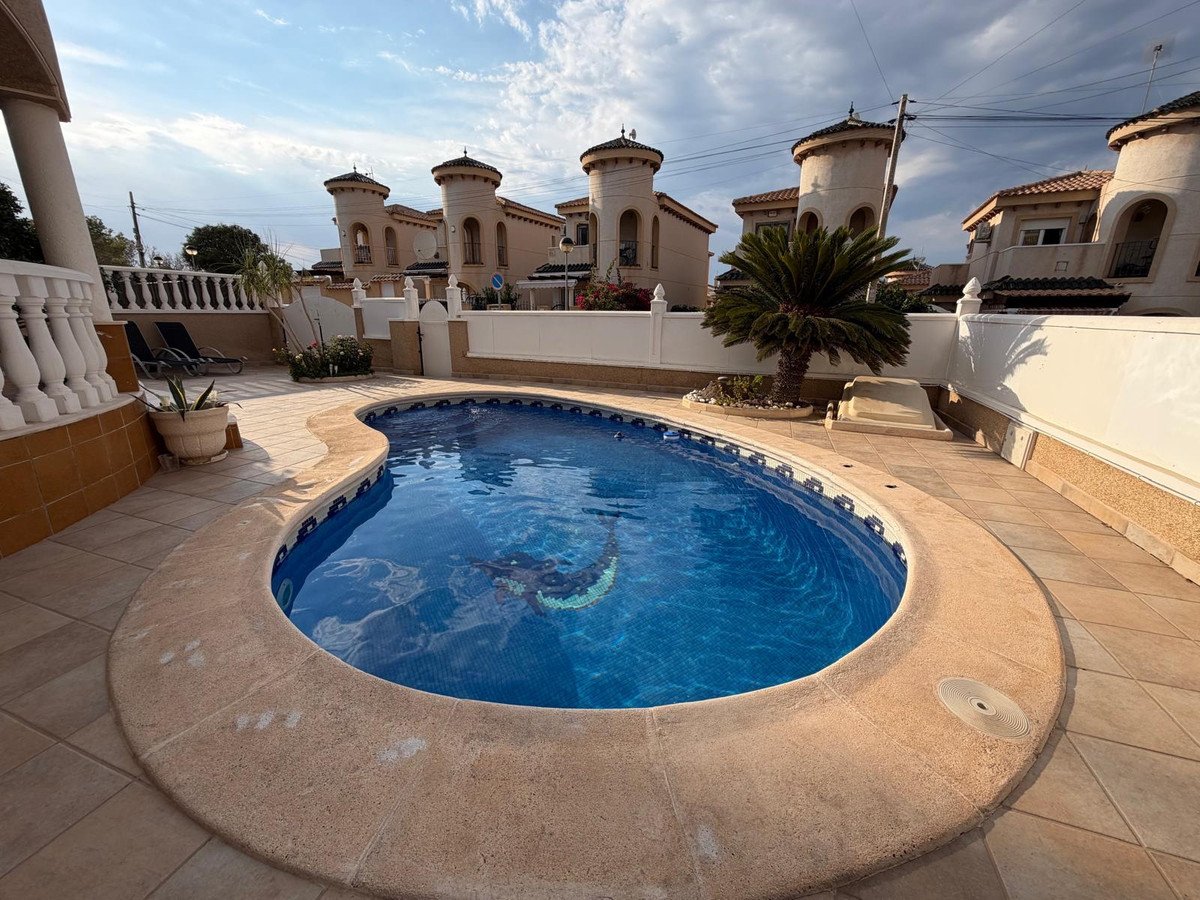 A luxurious private swimming pool with clear blue water, surrounded by a tiled patio and unique tower-style houses.