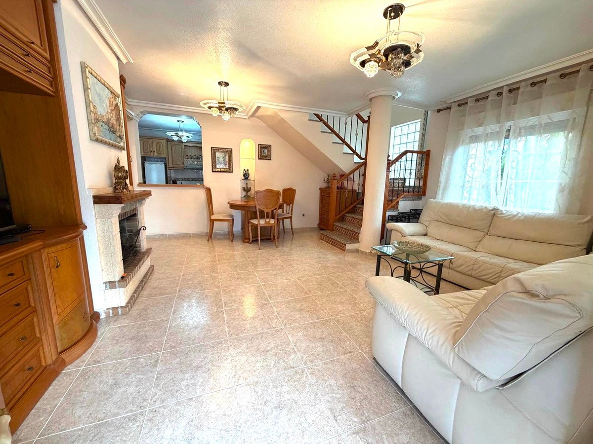 Living room with fireplace, cream sofa, dining area, and staircase. Natural light streams in through curtains.
