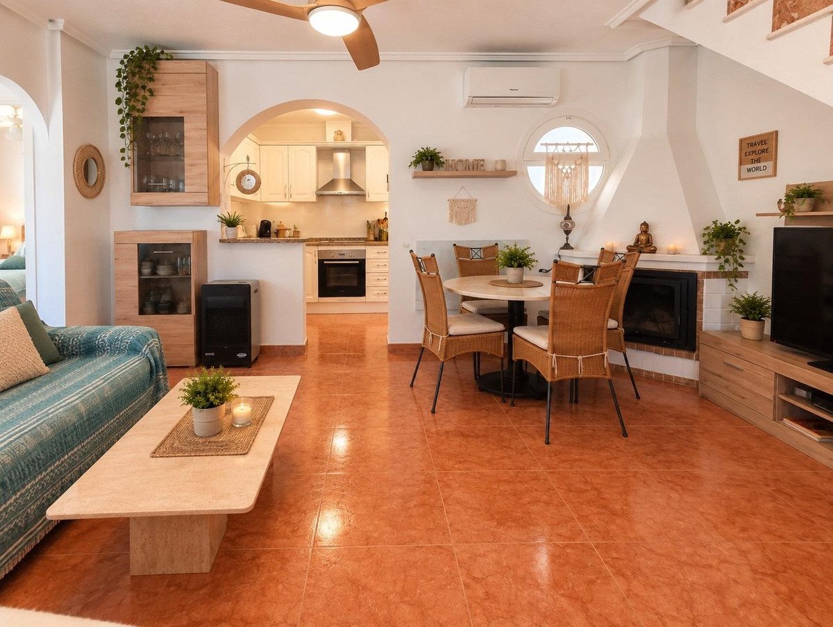 Living room with dining table, fireplace, and an open archway to a white kitchen with wood cabinets kitchen.