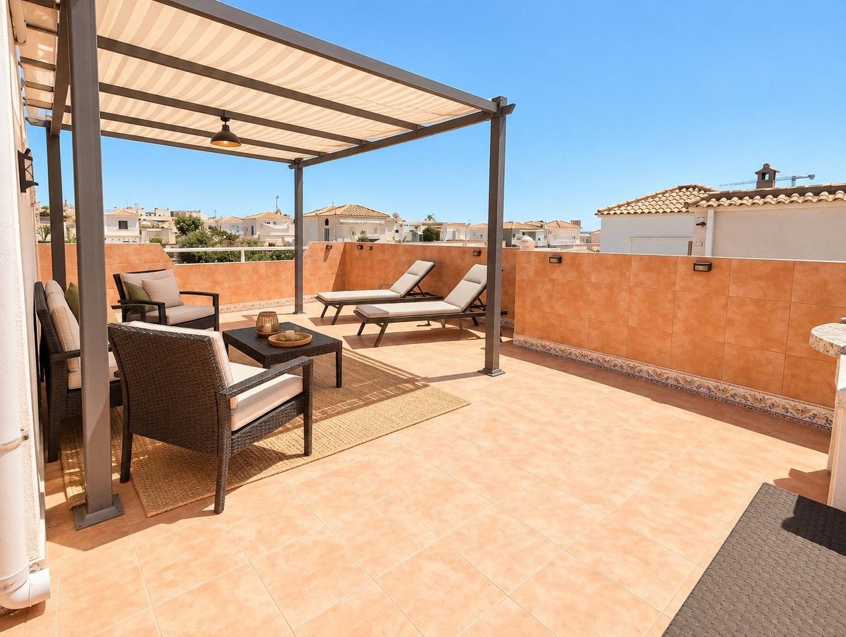 A spacious terrace with lounge chairs, seating area, coffee table, and a striped awning overhead, under a clear blue sky.