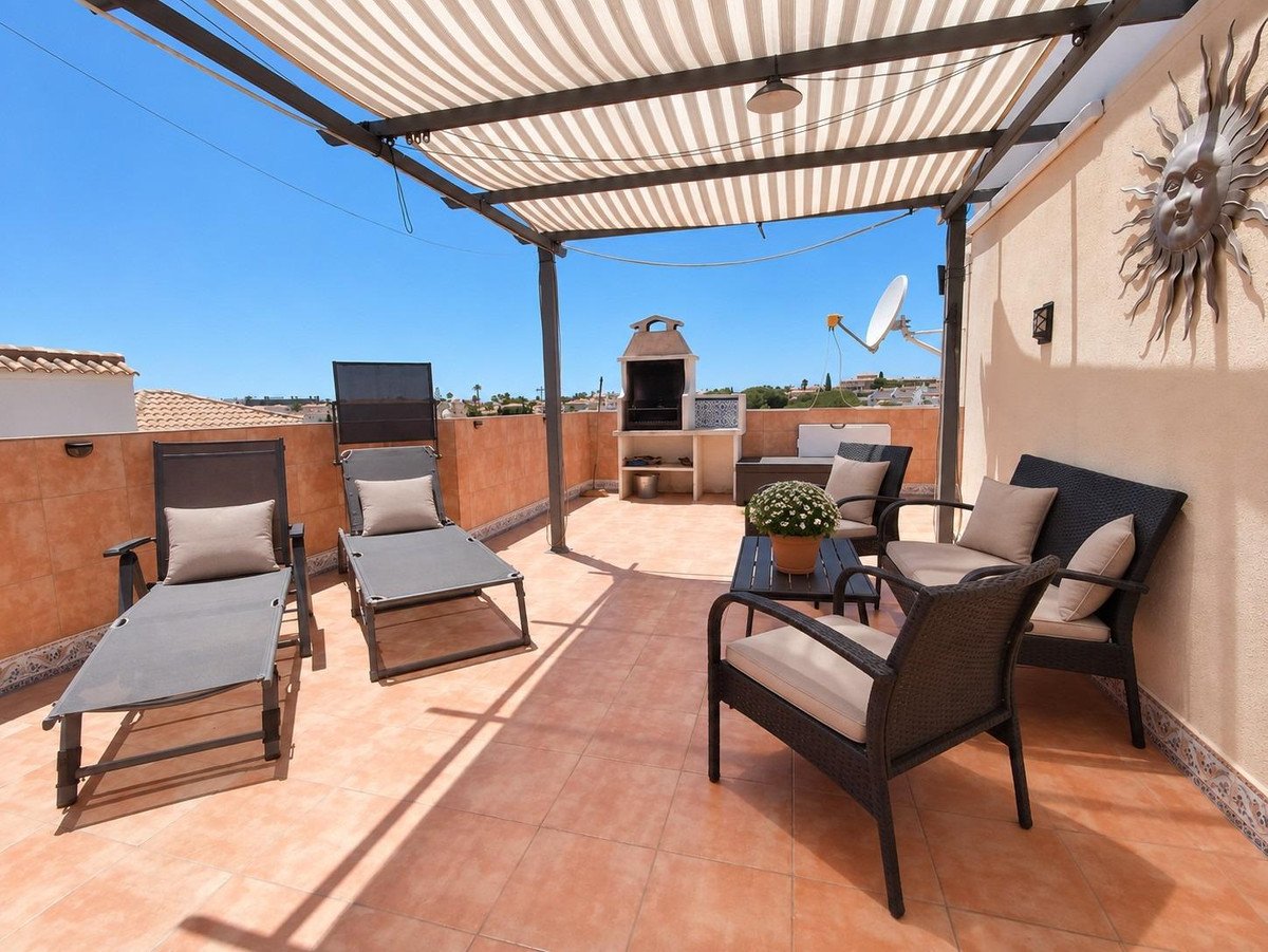 Outdoor terrace with sun loungers, seating area, barbecue, and sun-drenched views under a striped awning.