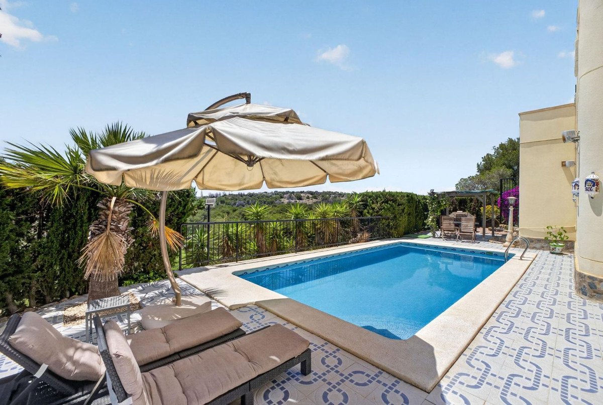 A private swimming pool with blue water, surrounded by a tiled patio, lounge chairs, and lush greenery, offering a relaxing outdoor space.