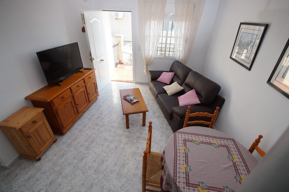Living room with a dark leather sofa, coffee table, TV, dining table, and access to a balcony.