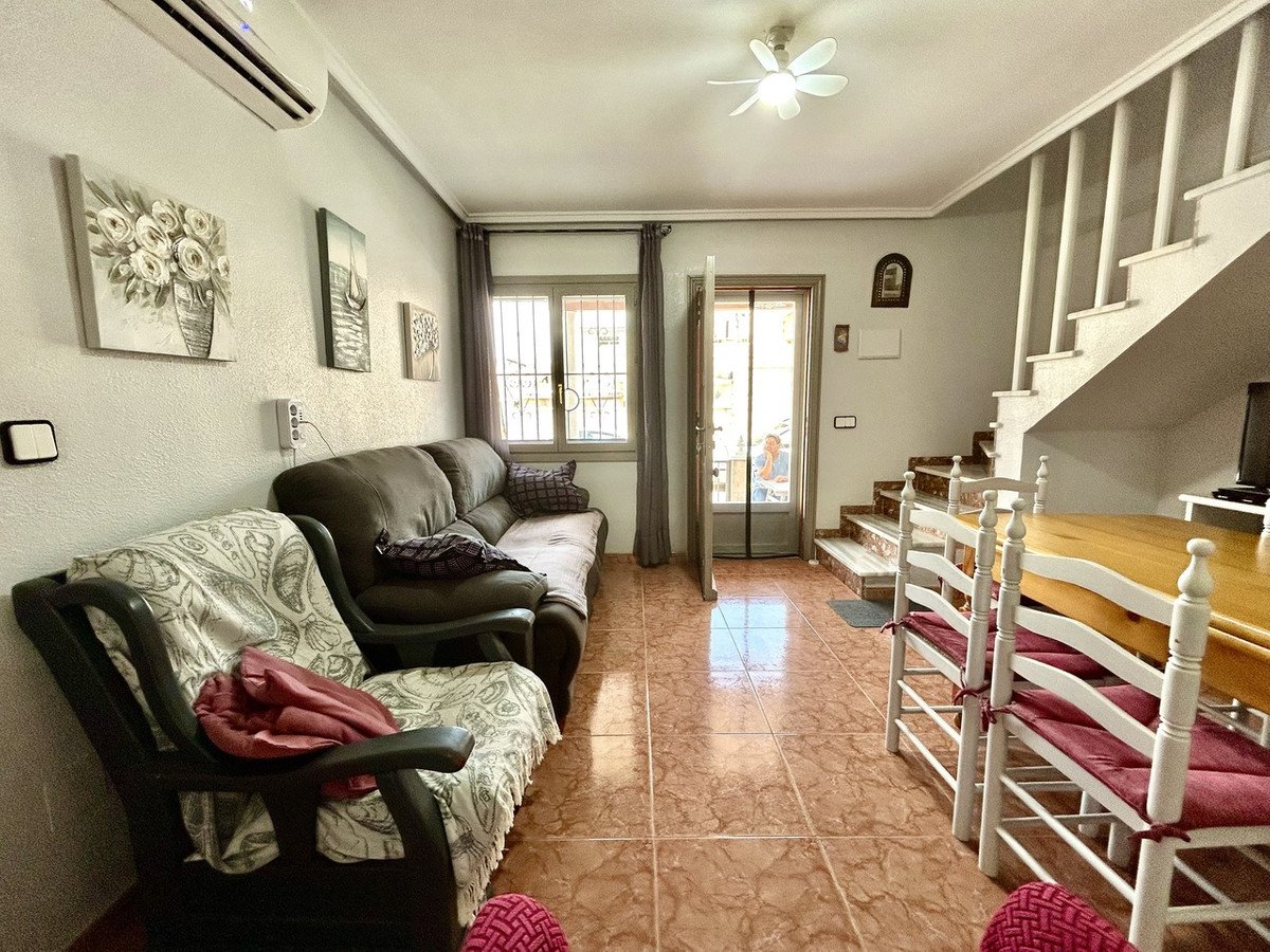 Cozy living area with a sofa, armchair, stairs, and a dining table. Features wall art and air conditioning.