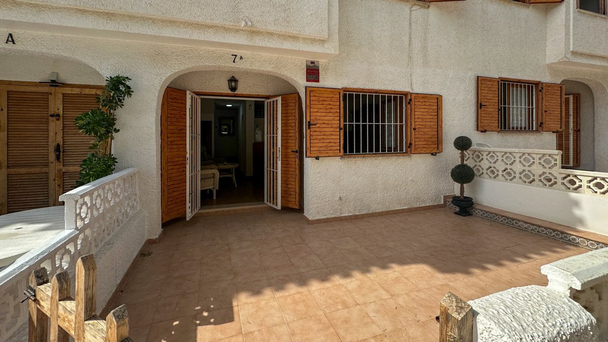 View of a tiled terrace with a double door entrance, windows with wooden shutters, and outdoor seating area.