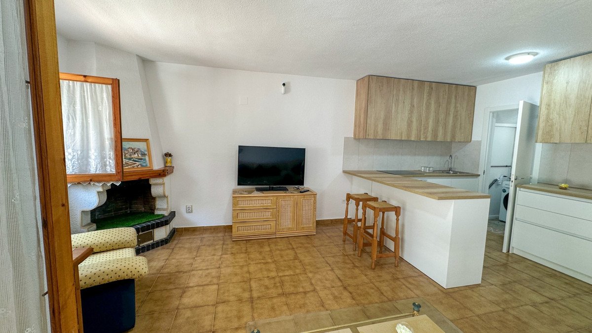 Living room with kitchenette, fireplace, TV, and bar stools. Open concept space with a glimpse of laundry area outside.