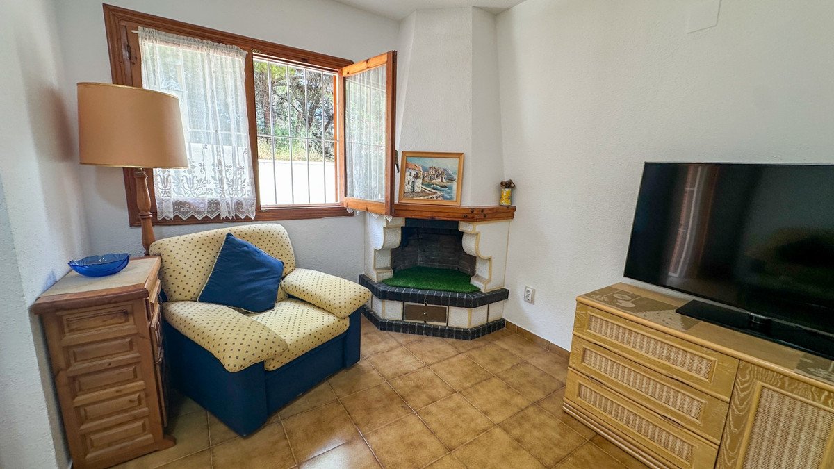 Living room with a comfortable armchair, a decorative fireplace, a television, and a window offering garden views.