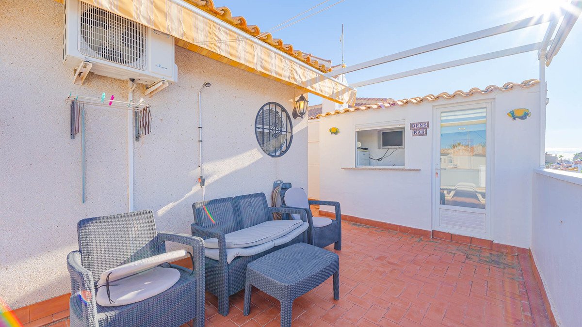 Rooftop terrace with wicker furniture, tiled floor, and ocean view under a clear sky.