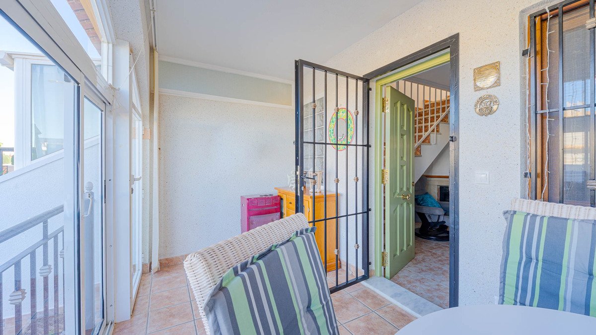 Balcony with wicker chairs, glass doors, and a view into a hallway with a green door and staircase.
