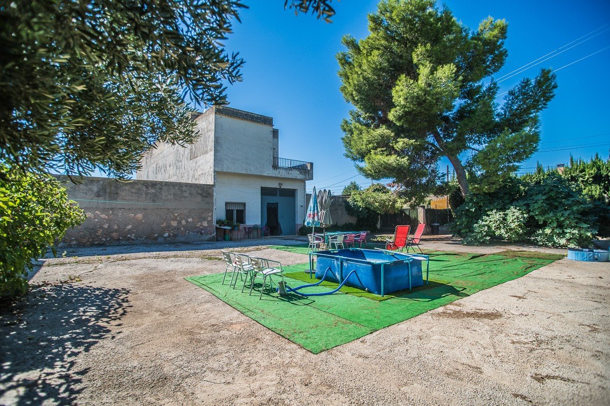 A small blue inflatable pool sits on artificial turf in the yard of a house on a sunny day.