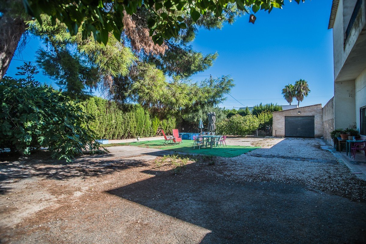 Sunny outdoor area with a swimming pool, patio furniture, trees, and a garage door. A garage is visible on the right side.