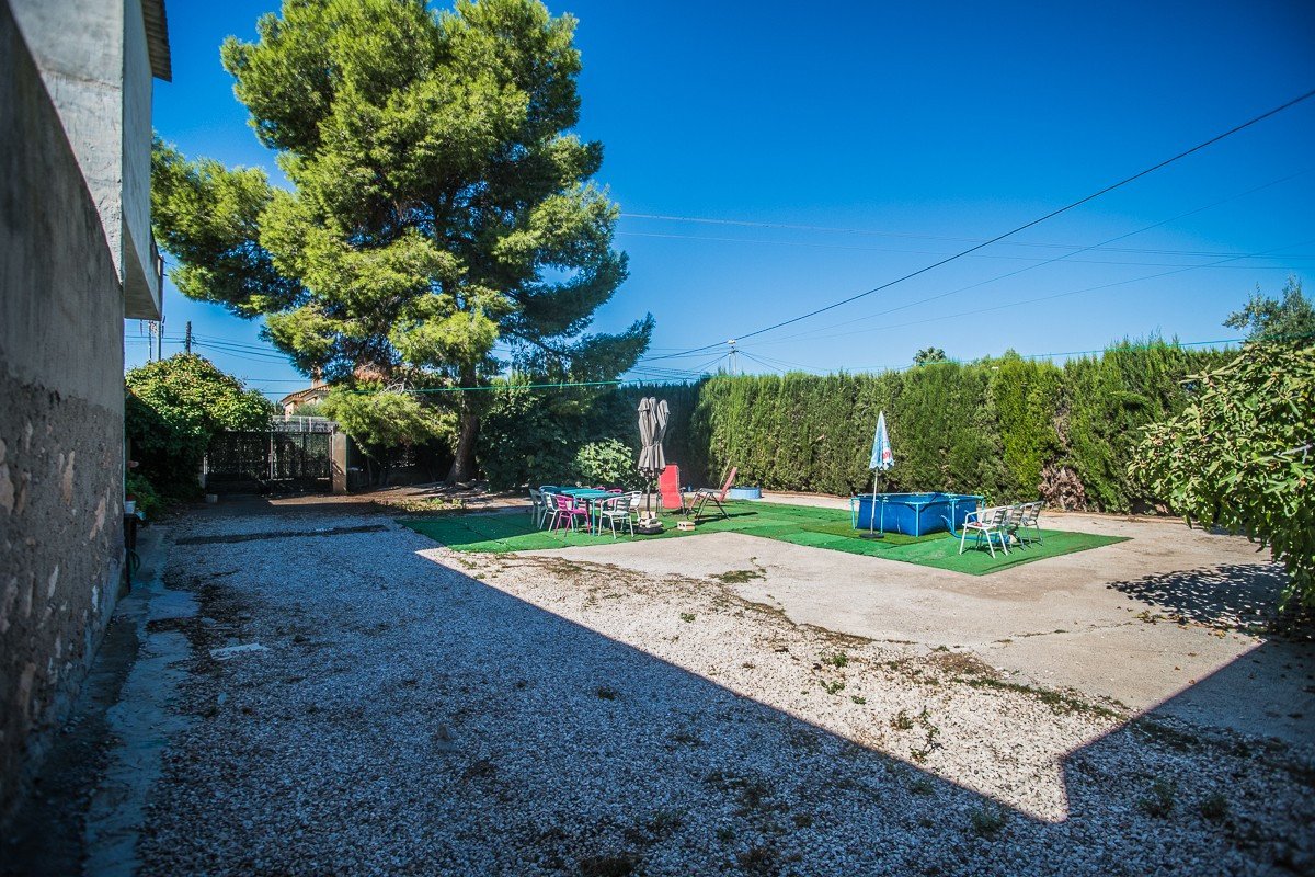 Outdoor backyard with a small blue pool, dining table and chairs, and lounge chairs under a large tree.