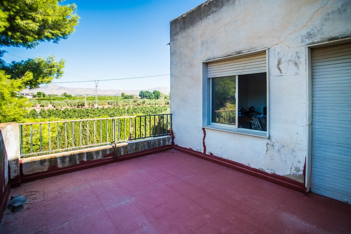 A terrace with a countryside view, featuring a railing and a window looking into a room.