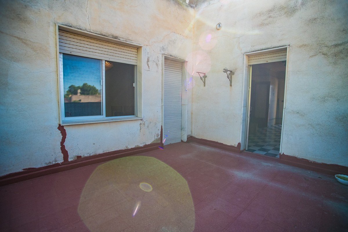 Outdoor terrace with a closed window, a closed door, and an open door leading to an interior with checkered flooring.