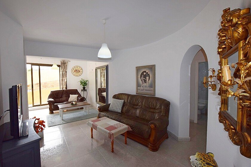 Living room with brown leather sofas, tiled floor, arched doorway, and large window view.