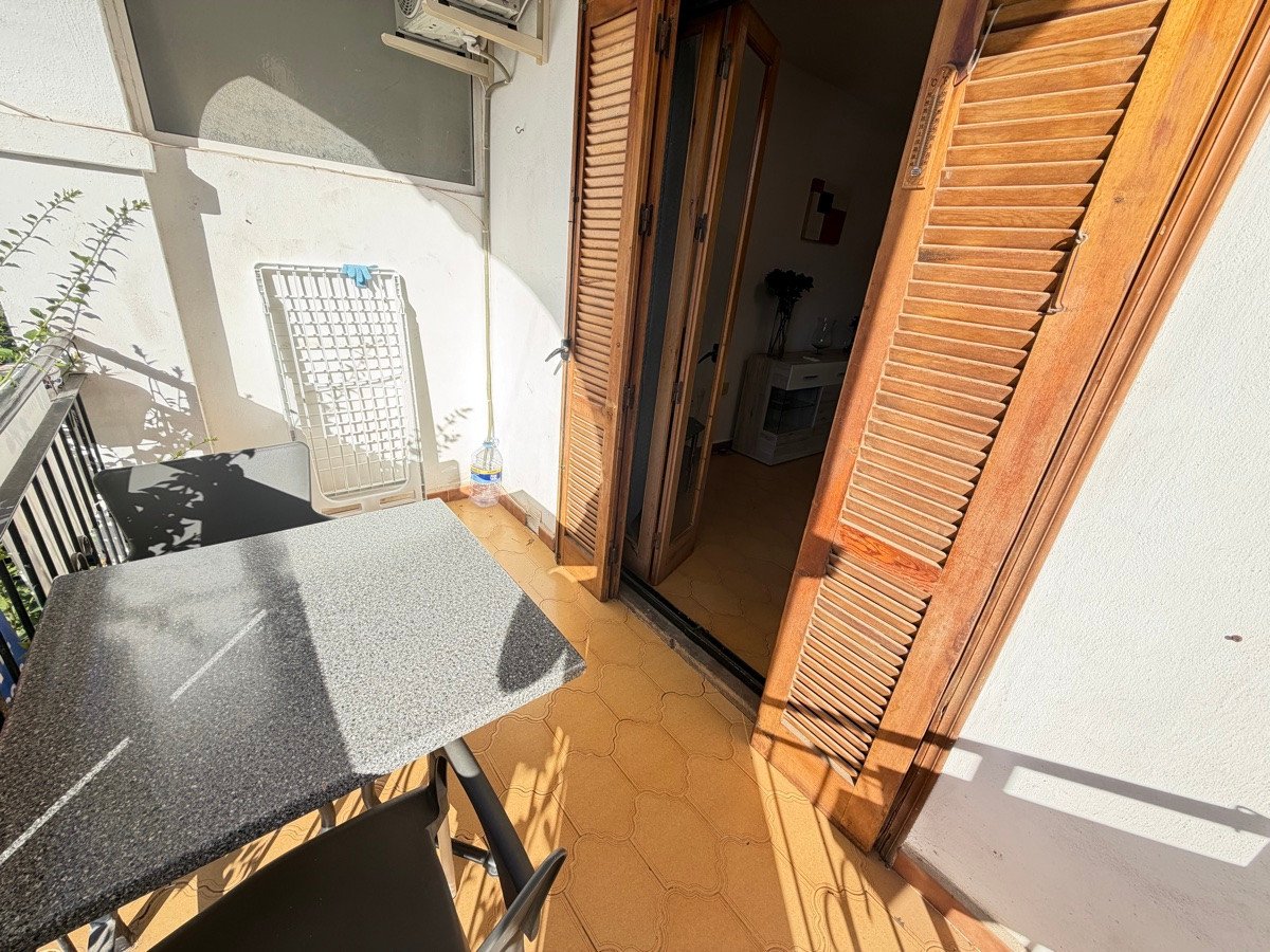 A small balcony with a table, chairs, and wooden shutters. An air conditioning unit is visible on the wall.