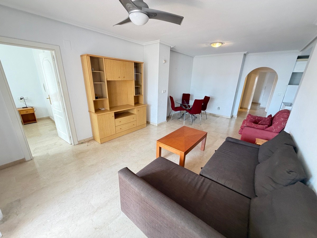 Living room with a dark sofa, red chairs around a dining table, and a wooden entertainment center.