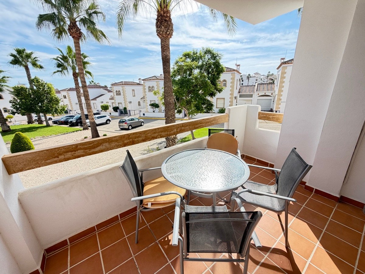 Terrace with table and chairs overlooking palm trees and residential buildings under a cloudy sky.