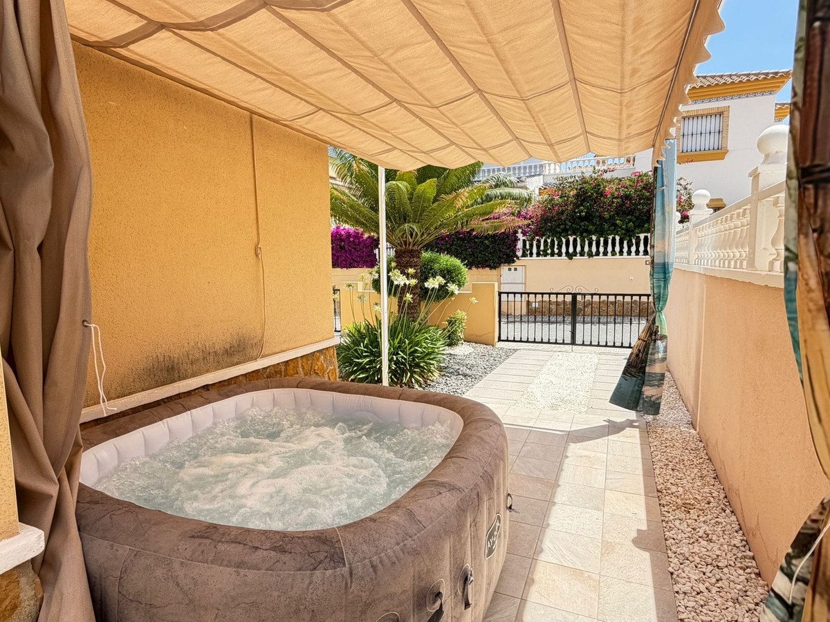 An inflatable jacuzzi sits outdoors on a tiled terrace, under a beige awning, surrounded by plants and a fence.