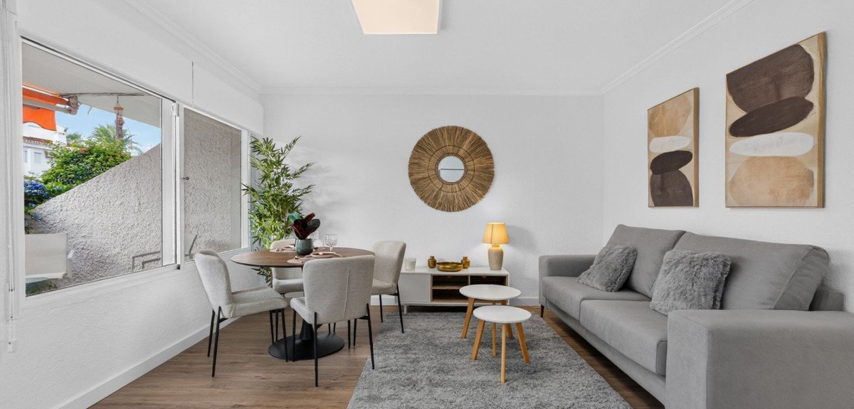 Spacious living and dining area with a grey sofa, round dining table, and large window view.