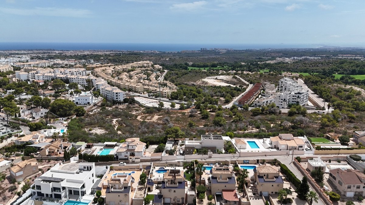 Aerial view of a residential area with houses and apartment buildings, lush greenery, and a distant view of the sea.