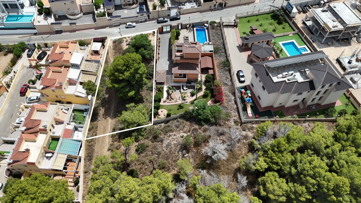 Aerial view of a villa with a swimming pool, garden, and surrounding trees, overlooking a residential area.