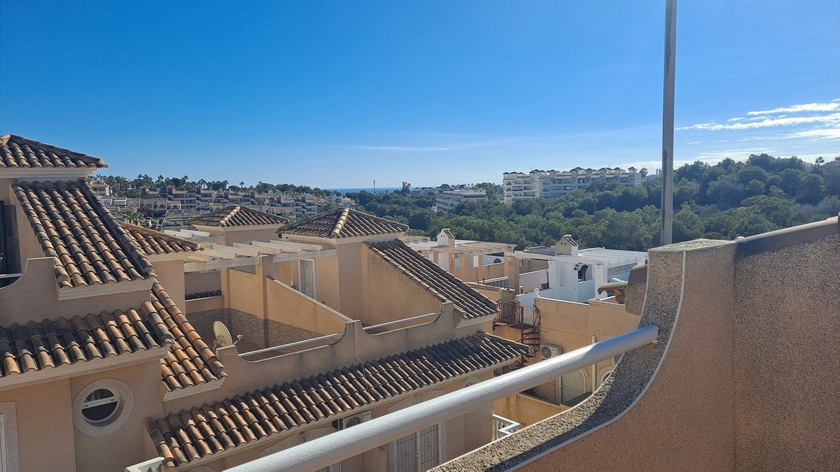 Balcony view of terracotta-tiled rooftops and distant sea under clear blue sky