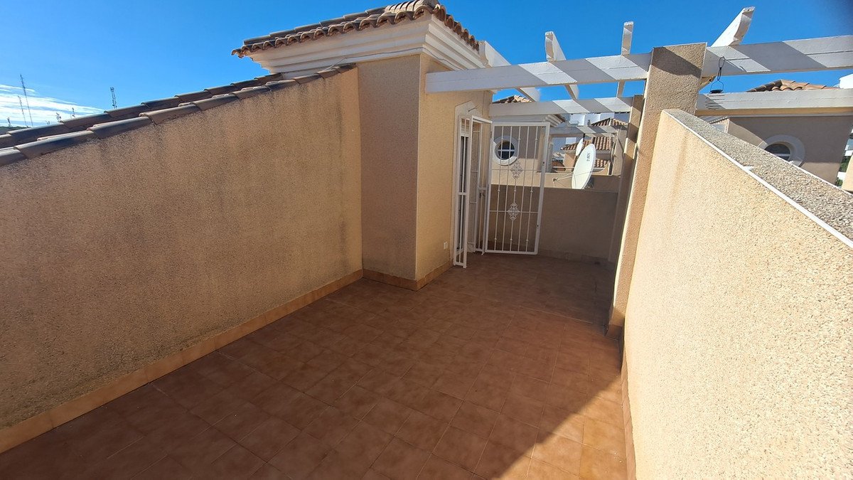 Rooftop terrace with tiled floor, beige walls, and white pergola under clear blue sky