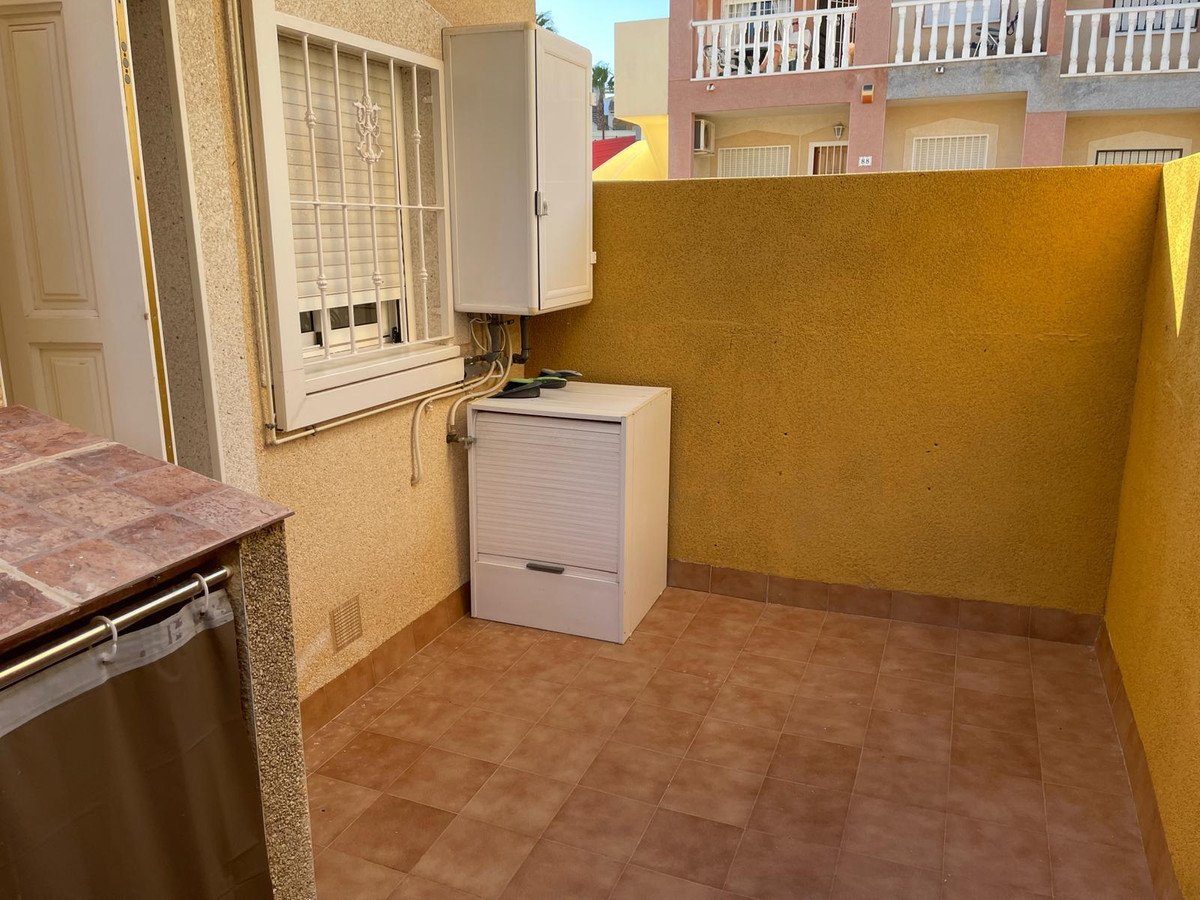 Small tiled terrace area with outdoor storage units and a yellow wall, featuring a barred window and a door.