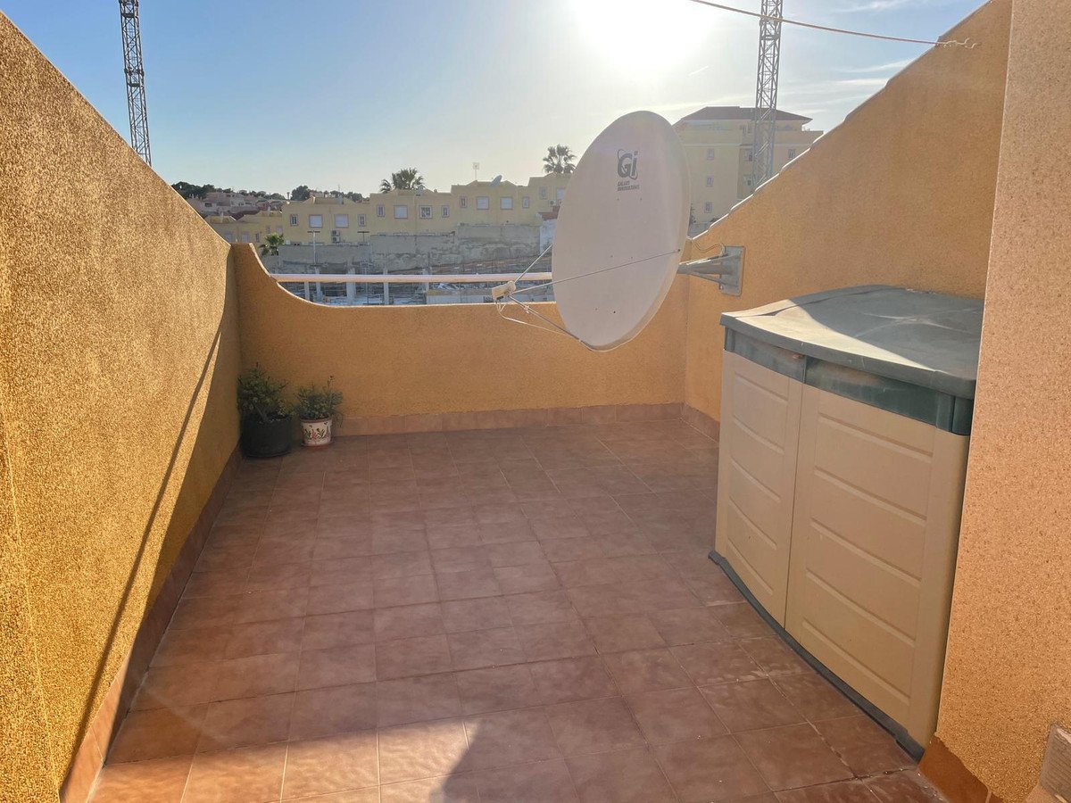 Sunny terrace with tiled floor, outdoor storage box, satellite dish, and a view of buildings.