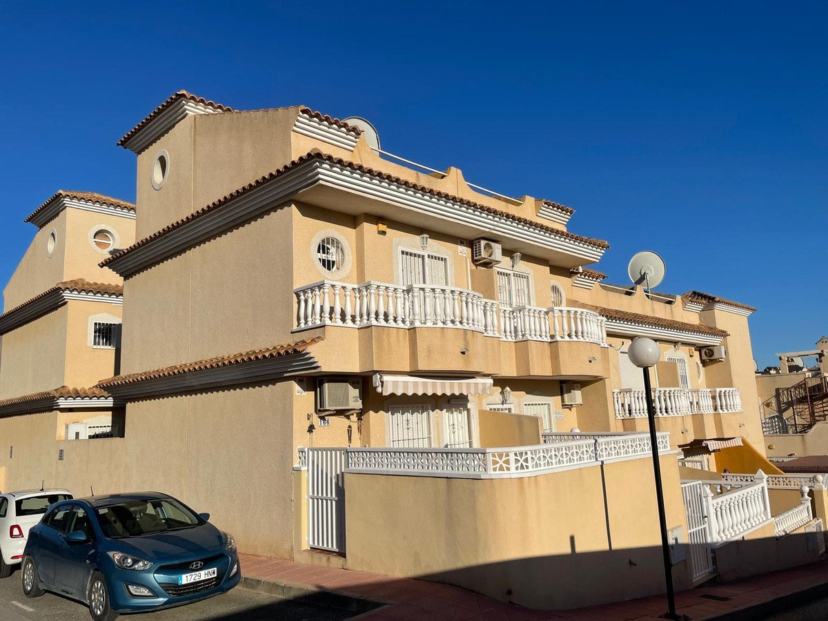 Exterior view of a light yellow multi-story house with white balconies, windows, and parking spaces in front.