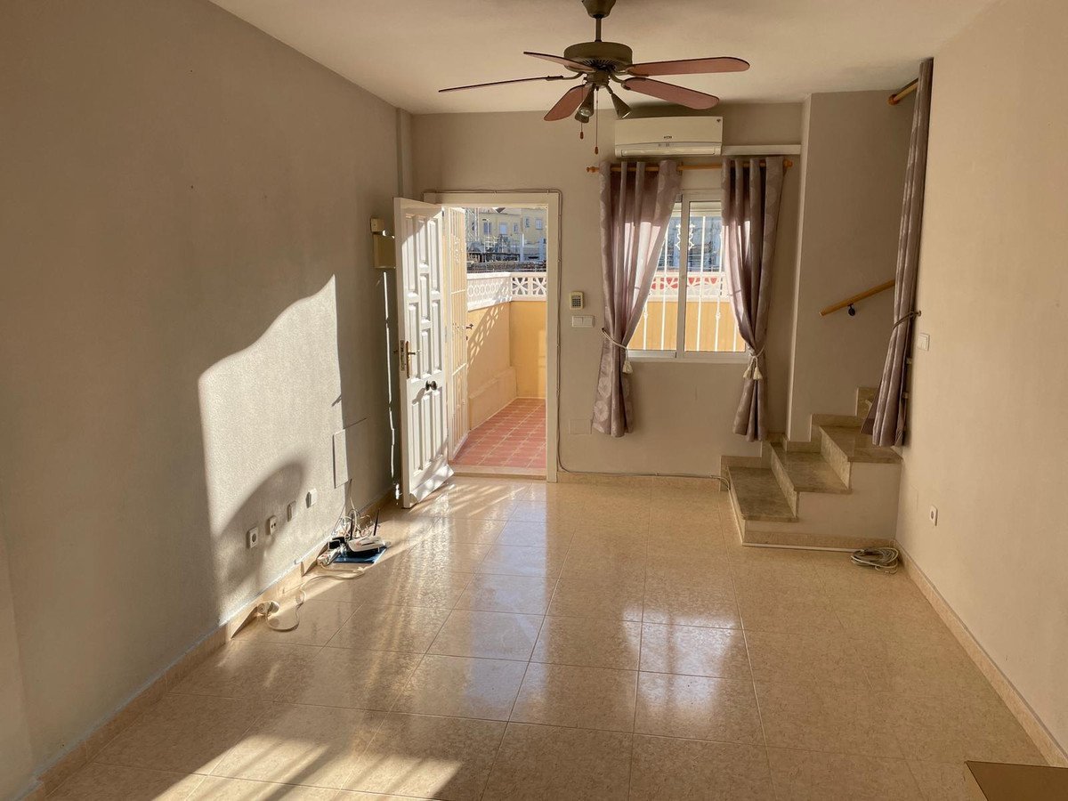 Interior living room with stairs, a ceiling fan, air conditioning unit, and doors opening to a sunny balcony.