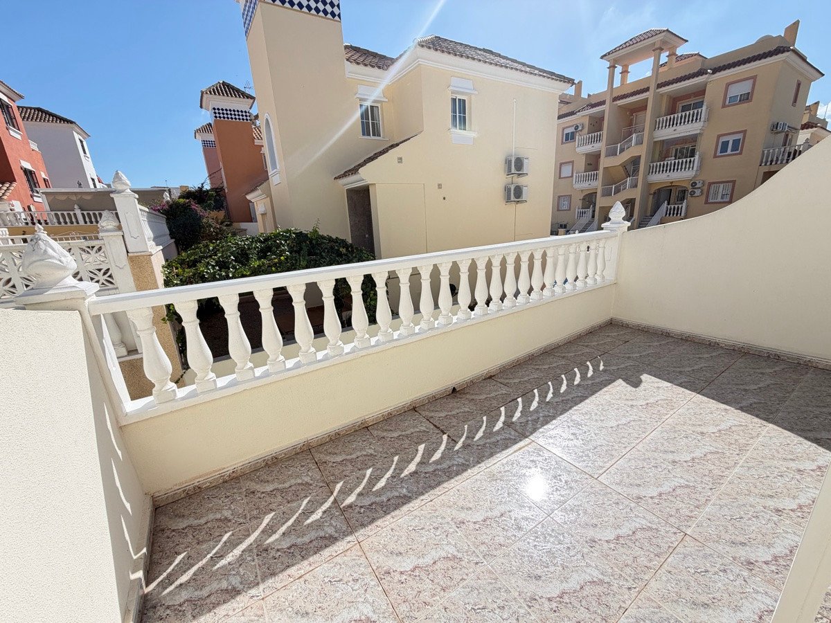 Terrace with white railing and tiled floor, overlooking residential buildings under a sunny sky.