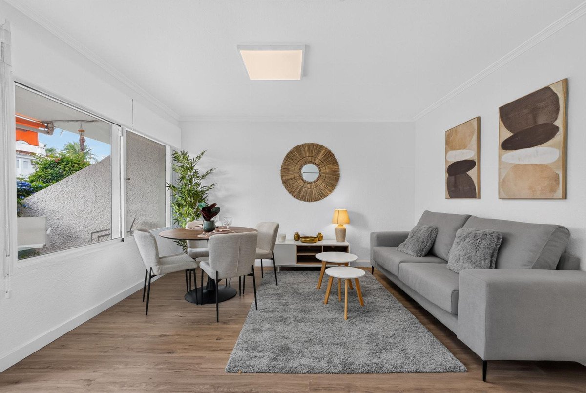 Modern living and dining area with neutral-toned furniture, large window, and artwork. Features a grey sofa and round dining table.
